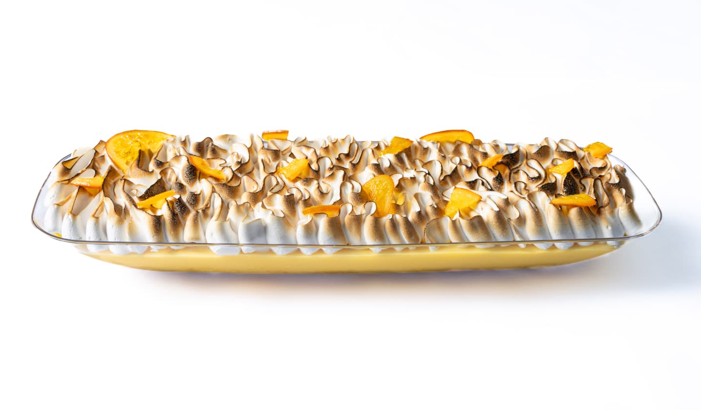 Long glass dish of toasted meringue dessert with orange slices on white