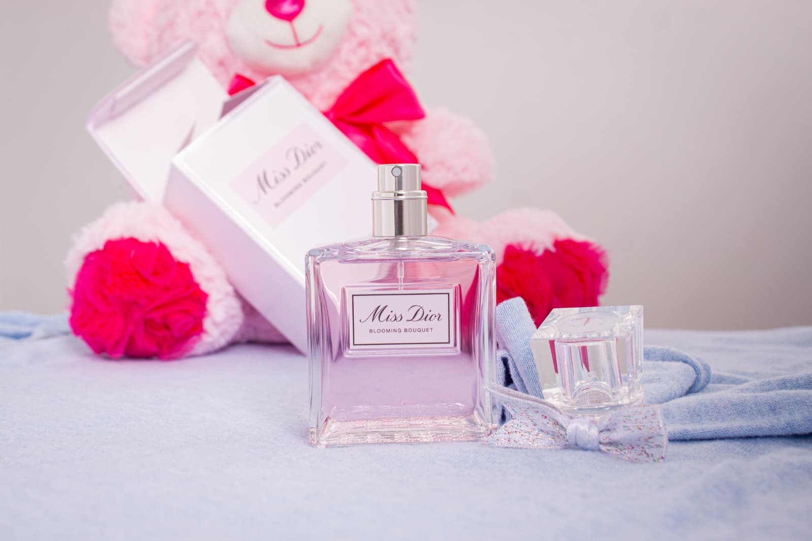 Perfume bottle styled with a pink teddy bear and blue fabric