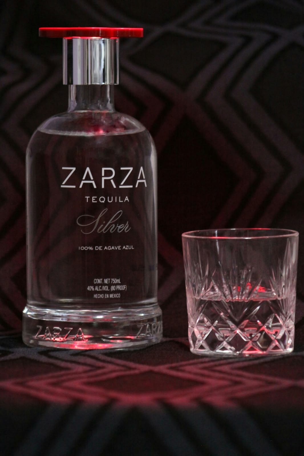 Zarza silver tequila bottle and cut-crystal glass with red light on dark patterned fabric