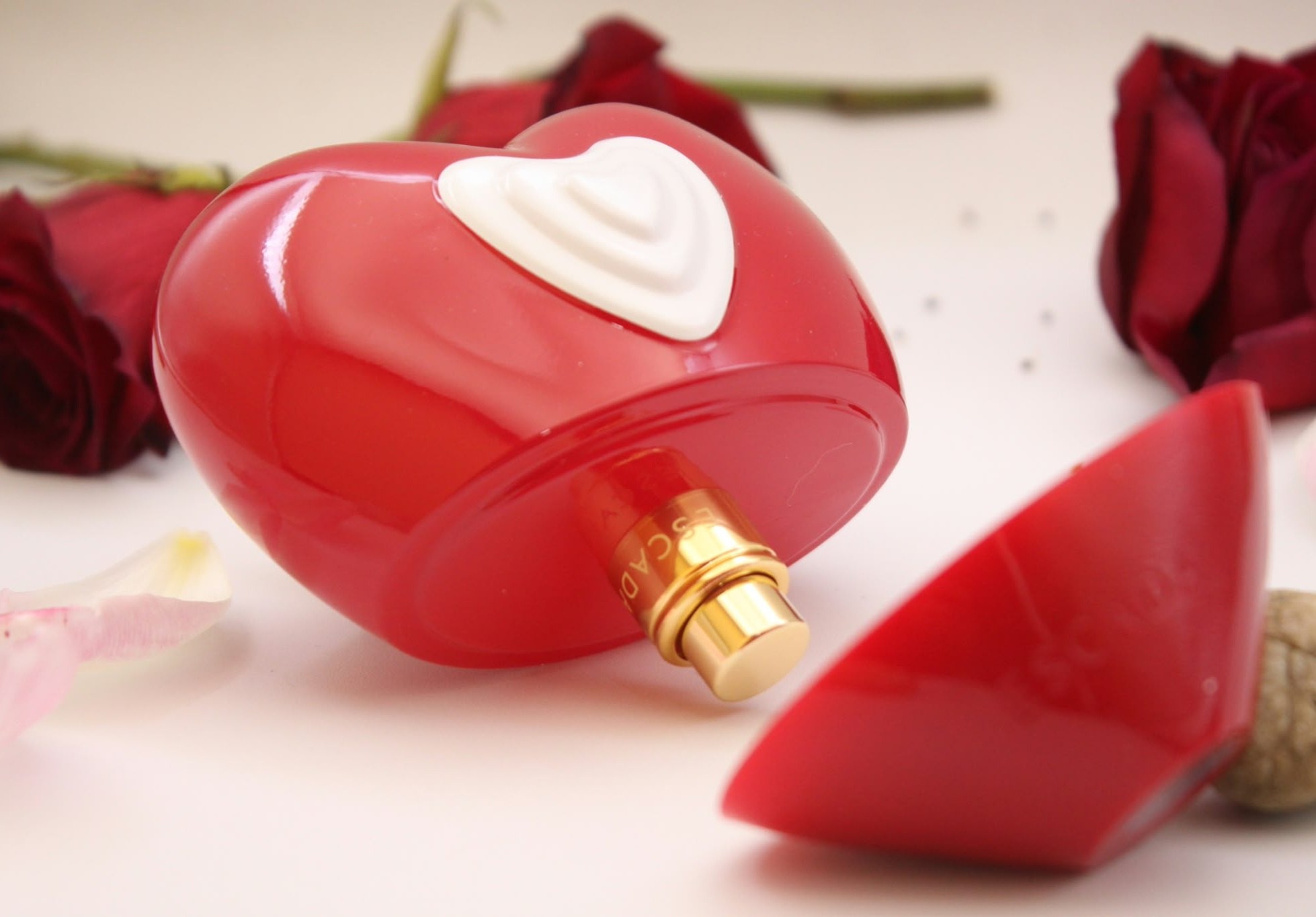 Red heart-shaped perfume bottle with a white heart detail, surrounded by red roses