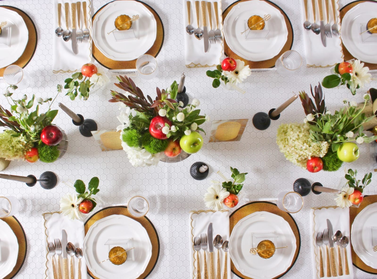 Overhead festive table setting with apples, flowers, gold chargers and black candlesticks